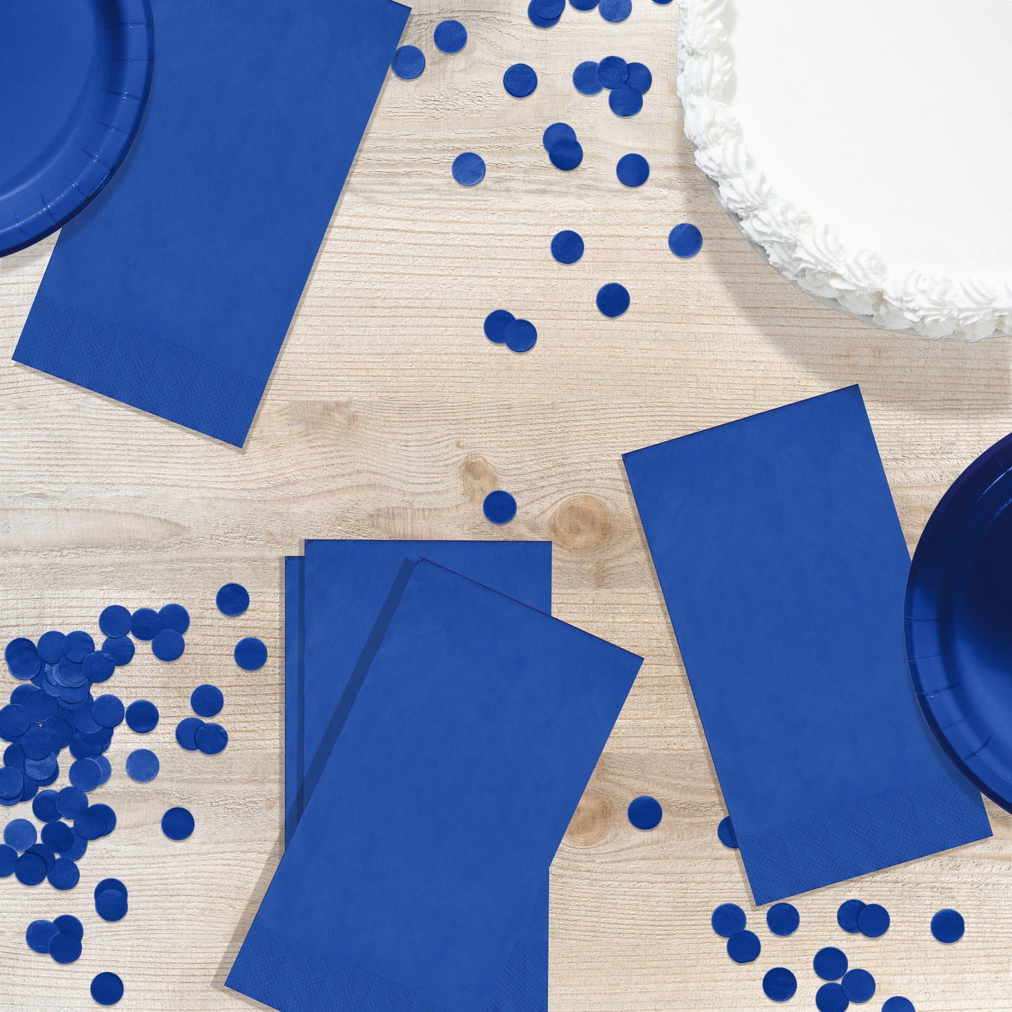 Blue party supplies including napkins, plates, and confetti on a wooden surface.