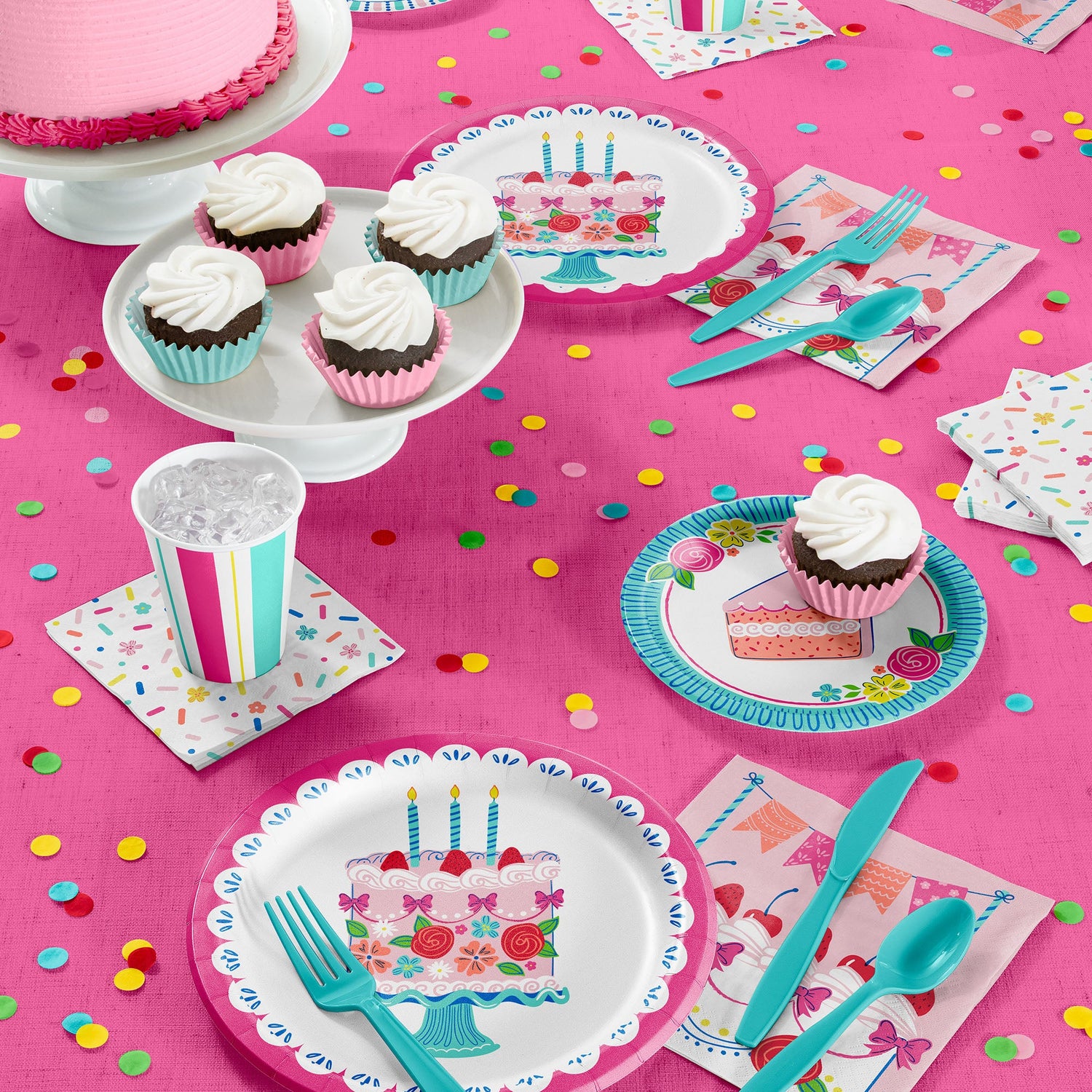 Pink and blue plates, napkins, cutlery on a pink tablecloth with cake and cupcakes