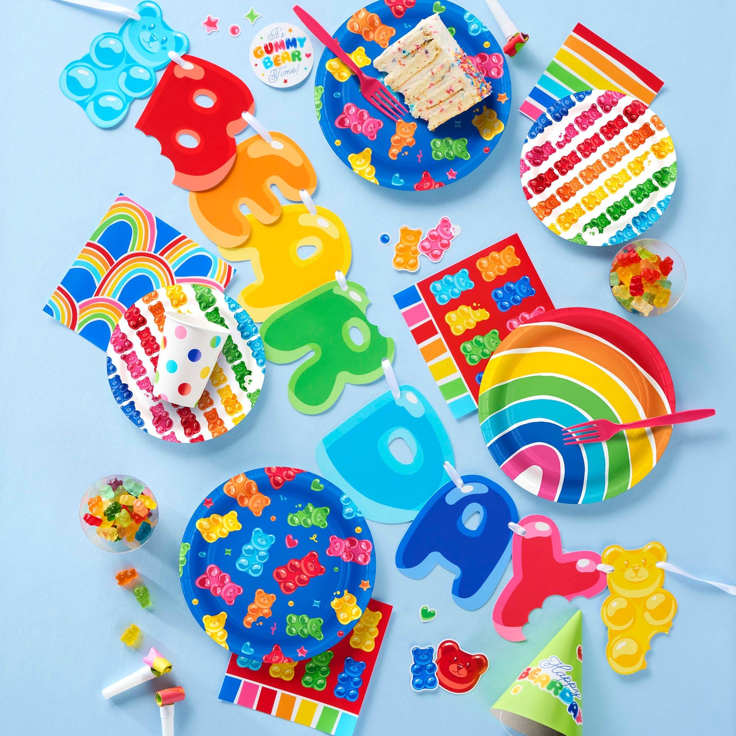 Colorful birthday party supplies including plates, cups, and decorations on a blue background.