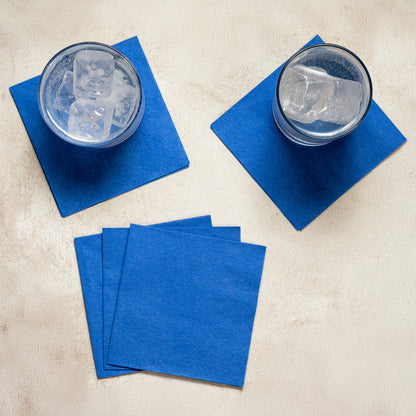 4.75" Regal Embossed Cobalt Blue Beverage Napkins 1000 ct displayed on a table with glasses of ice water