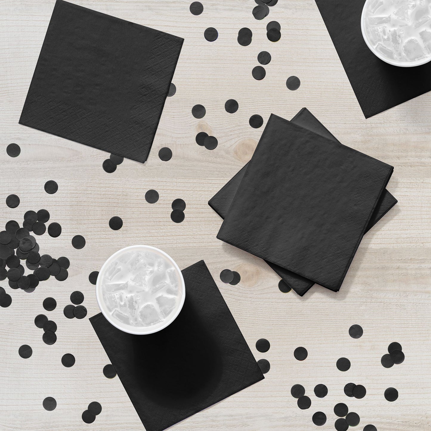 Black napkins and confetti on a light wooden surface