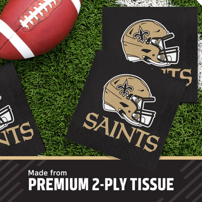 Black 2-ply tissue napkins featuring the New Orleans Saints helmet and 'SAINTS' text, arranged on green turf with a football prop. Text at the bottom reads 'Made from PREMIUM 2-PLY TISSUE'.