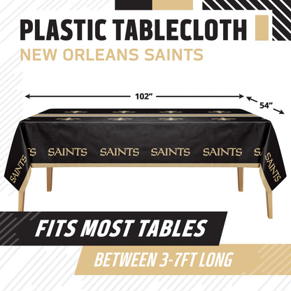 New Orleans Saints themed plastic tablecloth shown on a table with dimension arrows indicating 102 inches by 54 inches. The tablecloth is black with gold Saints logos and text.