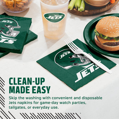 Green Jets-branded paper napkins with white logo graphics are shown on a table setting, alongside a matching drink cup, plate with a burger, fries, celery, and a fork resting on one napkin. Text on the image reads 'CLEAN-UP MADE EASY' and describes disposable Jets napkins for game-day or everyday use.
