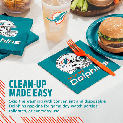 Teal Dolphins branded napkins, a matching cup, and an orange fork arranged on a table with a burger, celery, and fries. Text on the image reads 'CLEAN-UP MADE EASY' and describes disposable Dolphins napkins for game-day watch parties, tailgates, or everyday use.
