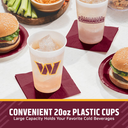 Two clear 20oz plastic cups with Washington Commanders branding are shown on dark red napkins at a table with burgers, celery, and bowls. Text at the bottom reads 'CONVENIENT 20oz PLASTIC CUPS Large Capacity Holds Your Favorite Cold Beverages.