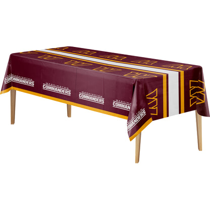 A rectangular table covered with a maroon, white, and yellow printed tablecloth. The cloth features repeated 'WASHINGTON COMMANDERS' text and team logos, with the team name also printed along the front edge.