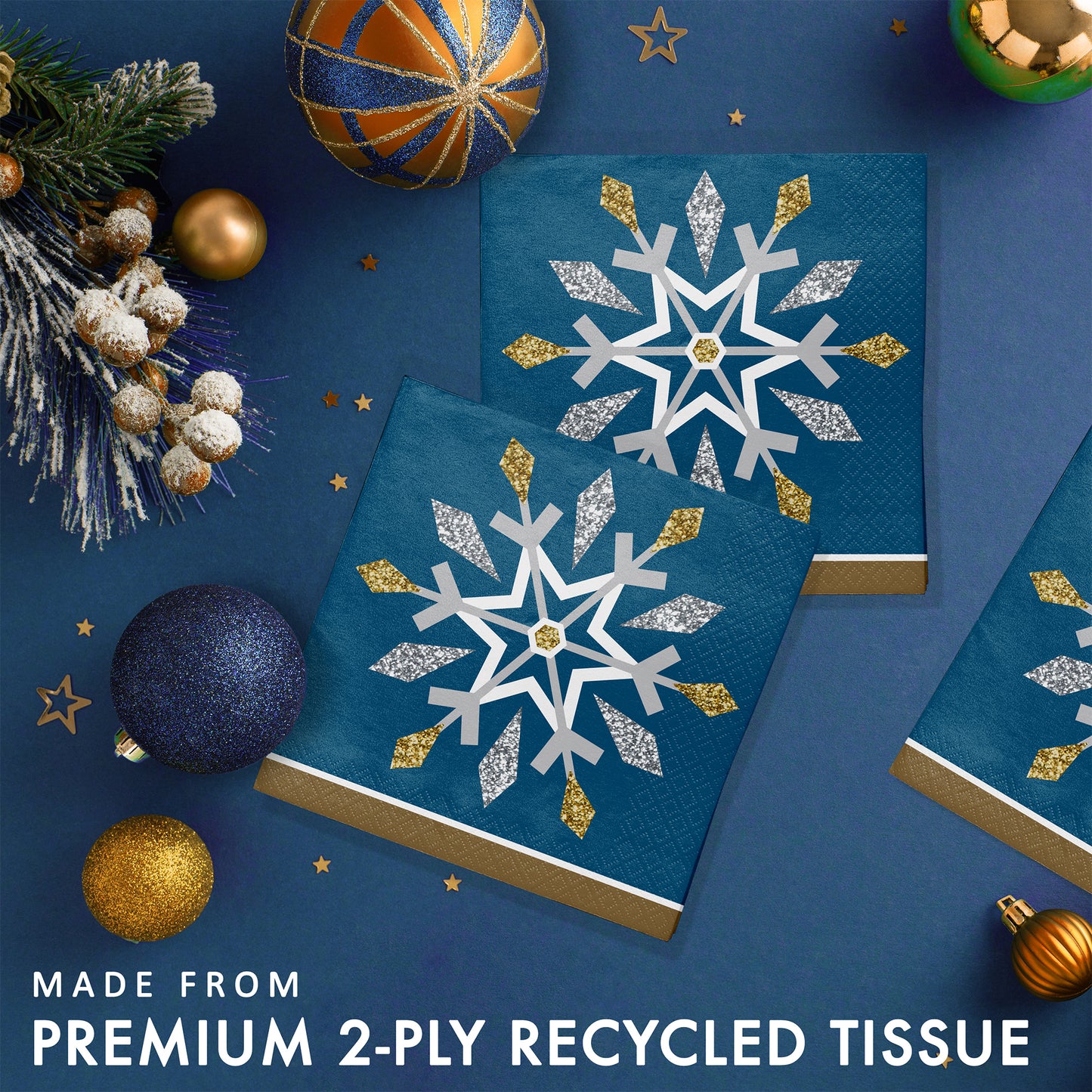 Blue paper napkins with snowflake design. Napkins are surrounded by Christmas ornaments on a blue background