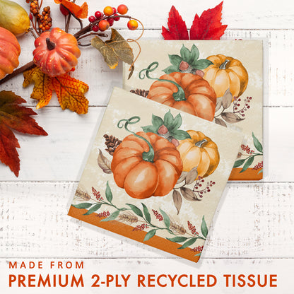 Harvest Delight Luncheon Napkins 192 ct. Two decorative paper napkins with pumpkin design on a white wooden surface with autumn leaves and berries.