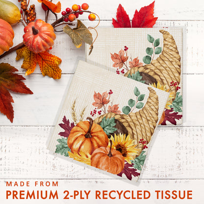 Fall Feast Luncheon Napkins 192 ct. Two decorative tissue papers with autumn designs on a white wooden surface with pumpkins and leaves.