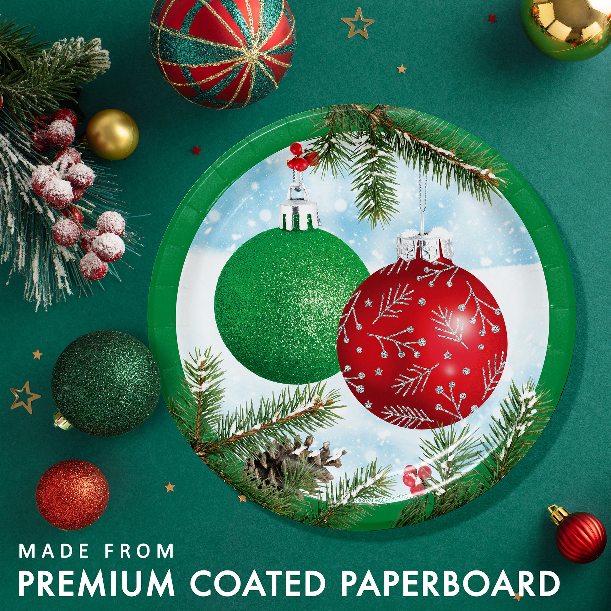 Decorative paper plate with Christmas ornaments on a green background surrounded by holiday decorations and greenery.