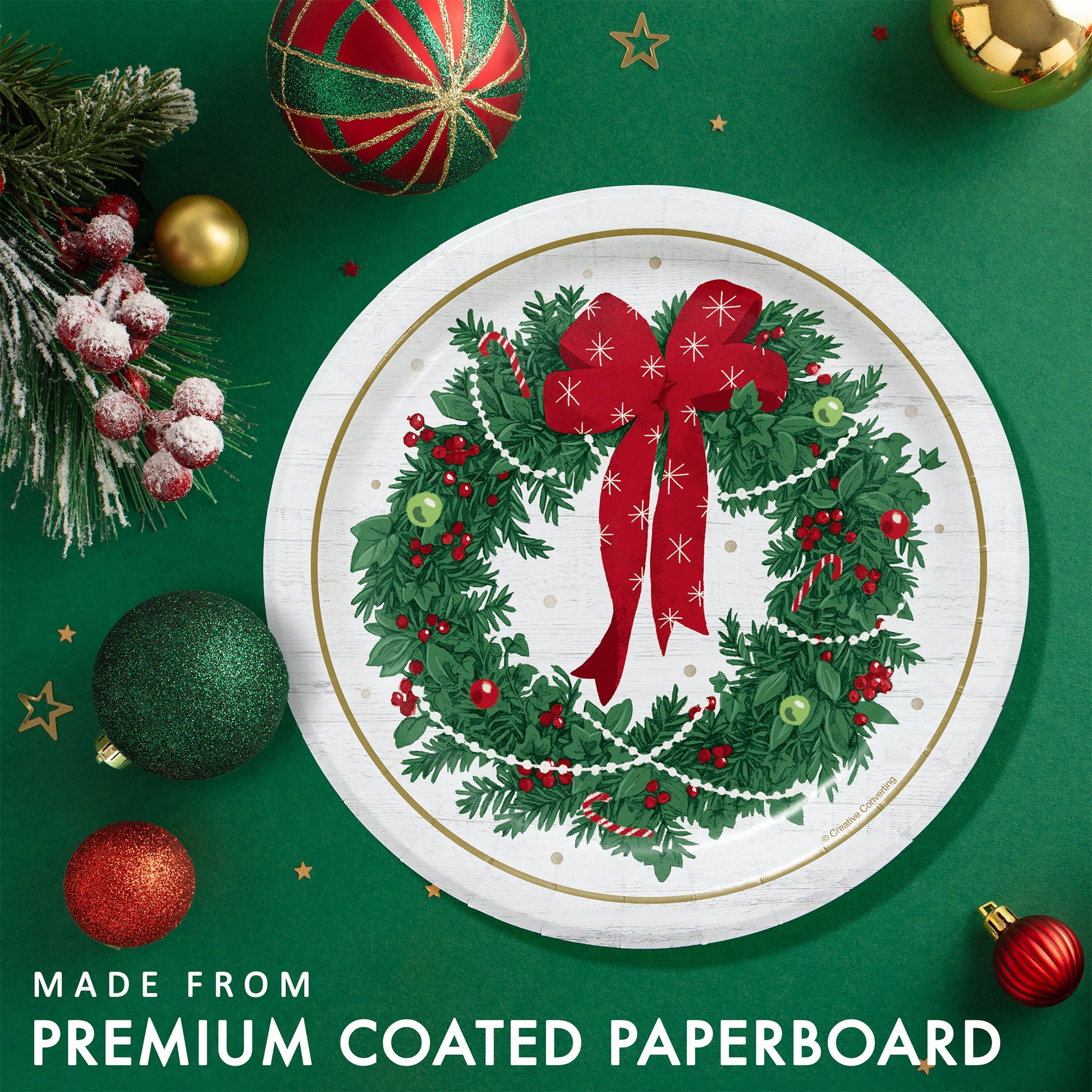 Christmas-themed paper plate with wreath design with a gold rim. Plate shown on a green background with festive decorations.