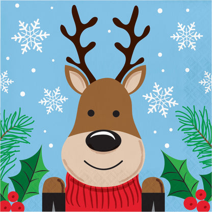 Christmas Cheer Luncheon Napkins 192 ct. Paper napkin featuring a cartoon reindeer with a red sweater on a blue background with snowflakes and greenery