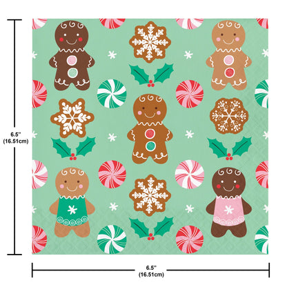 Christmas-themed paper napkin with gingerbread men, snowflakes, holly, and peppermints on a green background. Measurements included.