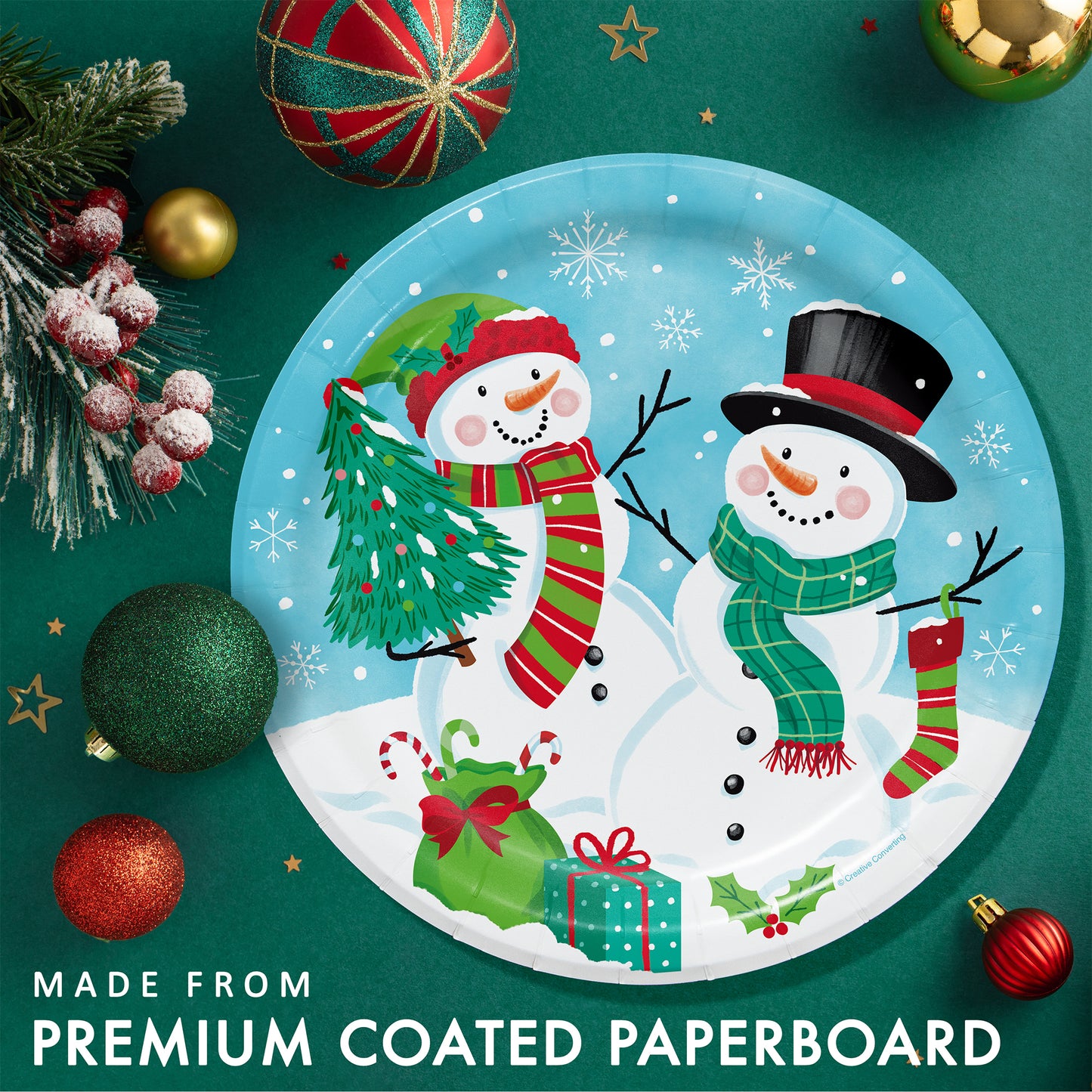 Frosty Friends Dinner Paper Plates 96 ct. Paper plate with 2 snowmen surrounded by Christmas presents and snowflakes. Shown on a green background with ornaments and greenery