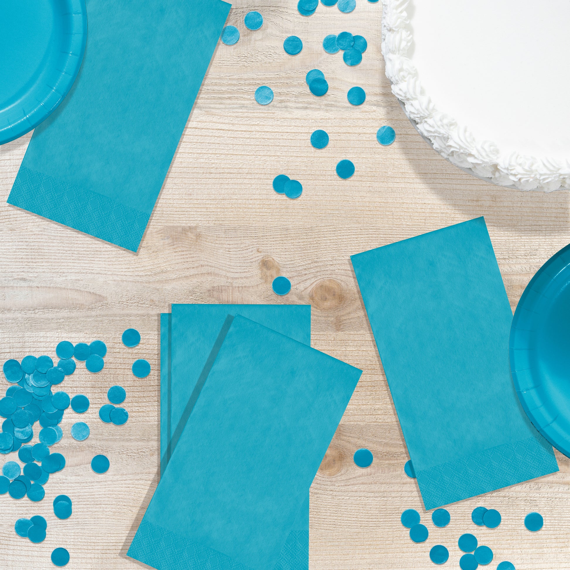 Blue party supplies including napkins, plates, and confetti on a wooden surface.