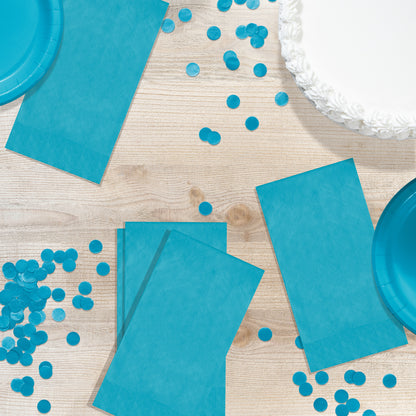 Blue party supplies including napkins, plates, and confetti on a wooden surface.