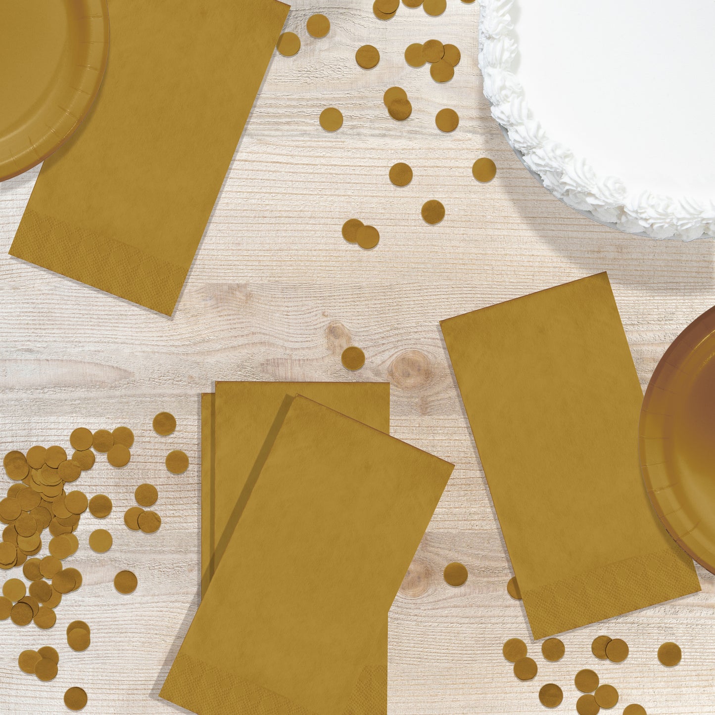 Gold paper plates and napkins with scattered gold confetti on a wooden surface