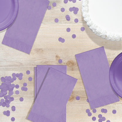 Purple party supplies including napkins and plates on a wooden surface with scattered purple confetti.