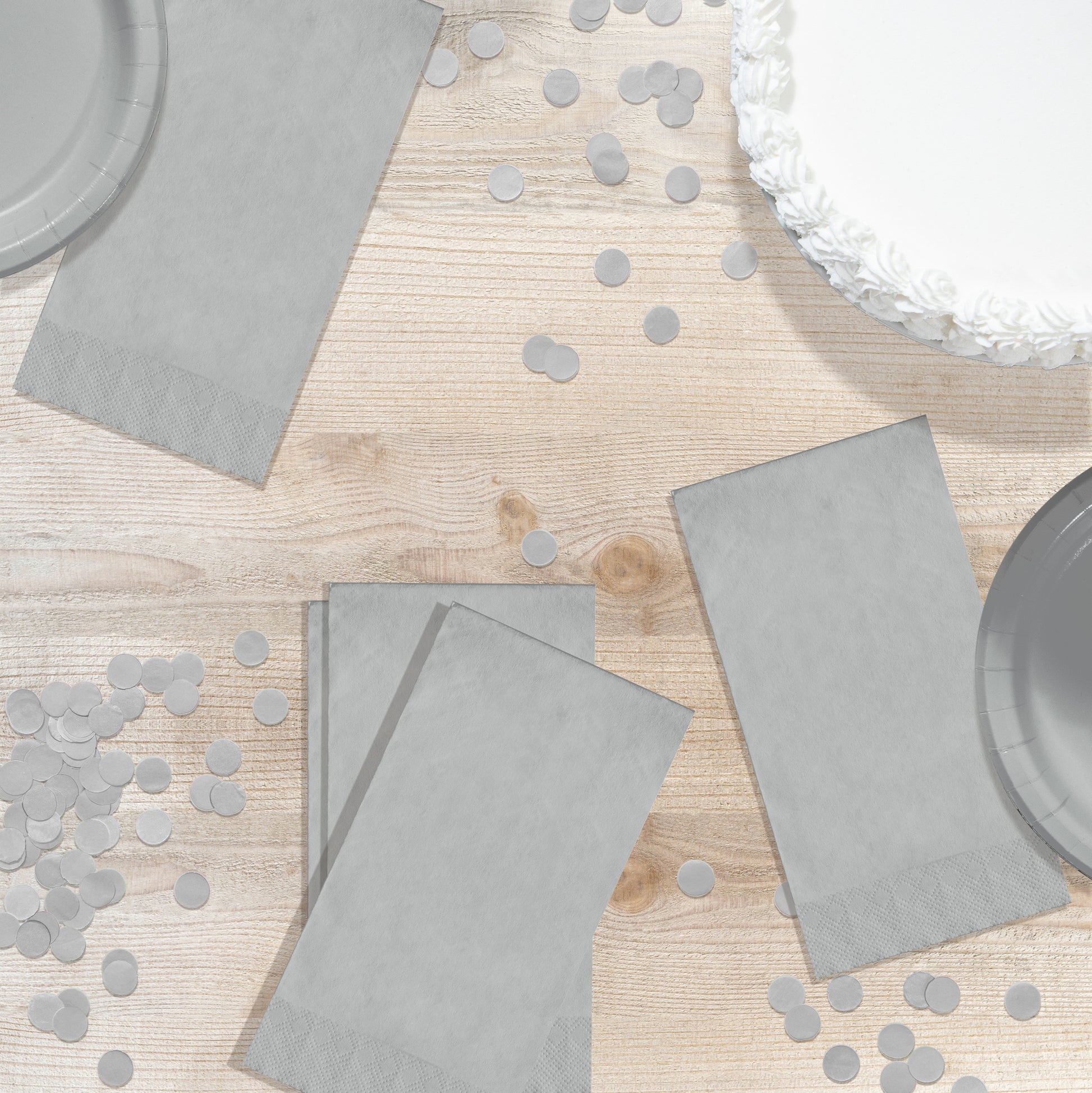 Gray paper plates and napkins on a wooden table with scattered confetti.