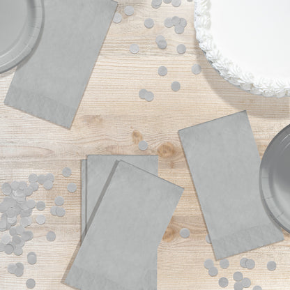 Gray paper plates and napkins on a wooden table with scattered confetti.