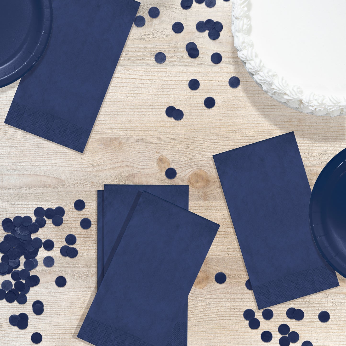 Navy blue party supplies including napkins, plates, and confetti on a wooden surface.