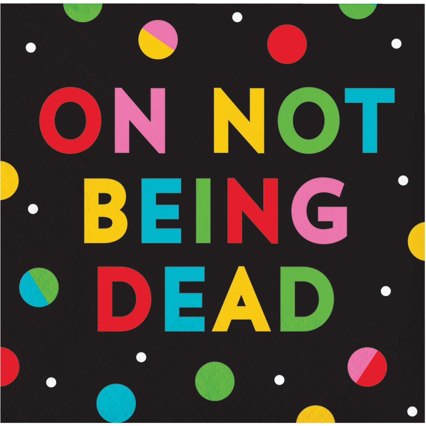 Napkin with colorful text 'ON NOT BEING DEAD' on a black background with polka dots.