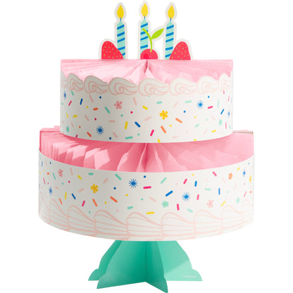 Two-tiered birthday cake paper centerpiece with pink frosting, colorful sprinkles, and candles on a white background.
