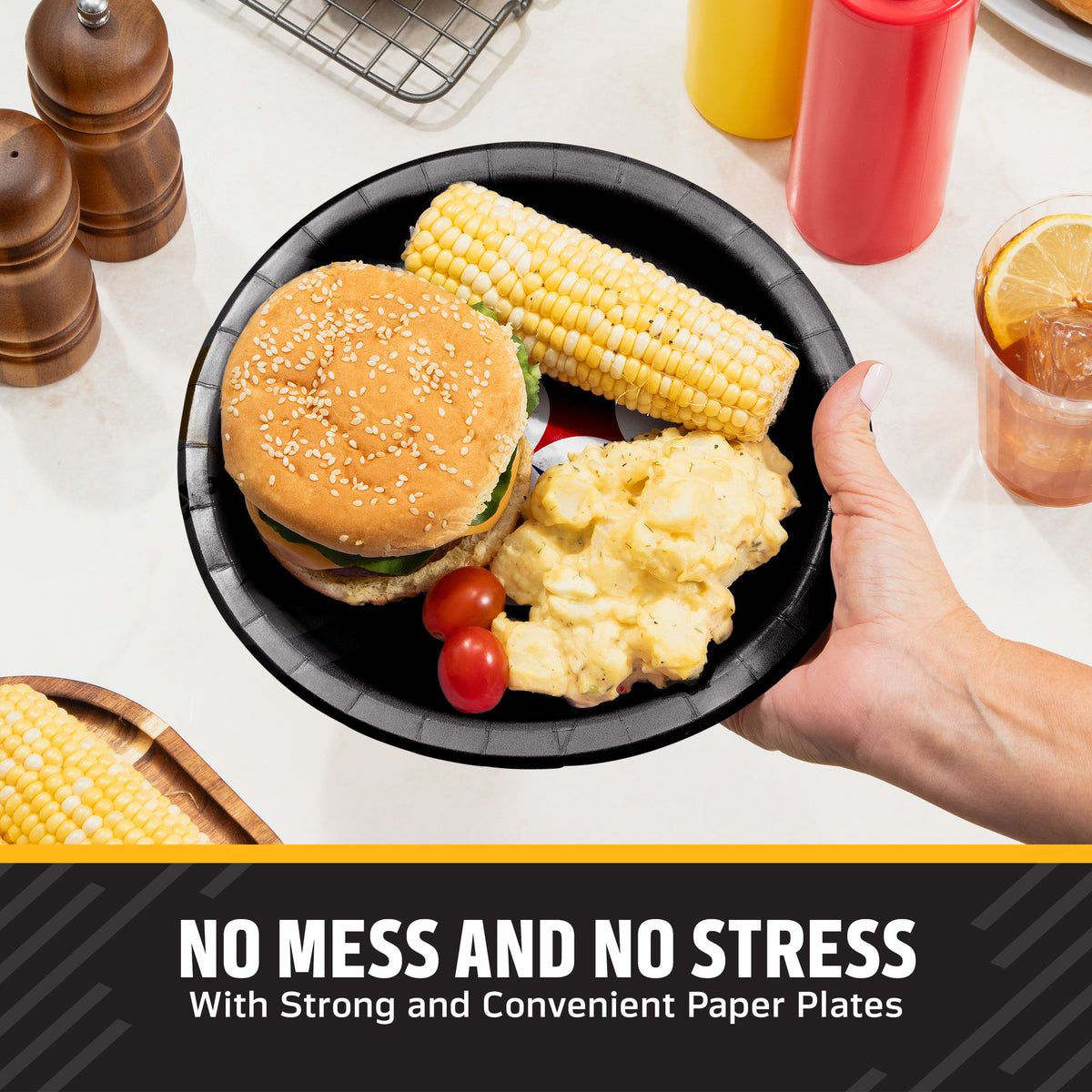 A hand holds a black Pittsburgh Steelers paper plate with a hamburger, corn on the cob, potatoes, and cherry tomatoes on a kitchen counter. Condiment bottles, pepper mills, and a drink are visible in the background, with the text 'NO MESS AND NO STRESS With Strong and Convenient Paper Plates' at the bottom.