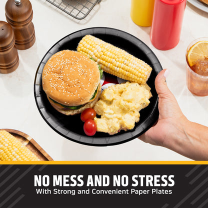 A hand holds a black Pittsburgh Steelers paper plate with a hamburger, corn on the cob, potatoes, and cherry tomatoes on a kitchen counter. Condiment bottles, pepper mills, and a drink are visible in the background, with the text 'NO MESS AND NO STRESS With Strong and Convenient Paper Plates' at the bottom.