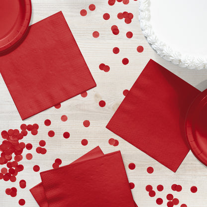 Red paper napkins and plates with red confetti on a white wooden surface