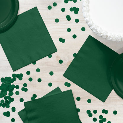 Green napkins and paper plates with green confetti on a light wooden surface