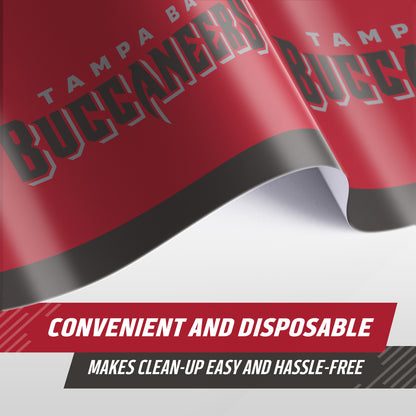 A close-up of a red Tampa Bay Buccaneers tablecloth, showing text along the edge saying 'TAMPA BAY BUCCANEERS'. A promotional banner at the bottom reads 'CONVENIENT AND DISPOSABLE' and 'MAKES CLEAN-UP EASY AND HASSLE-FREE'.