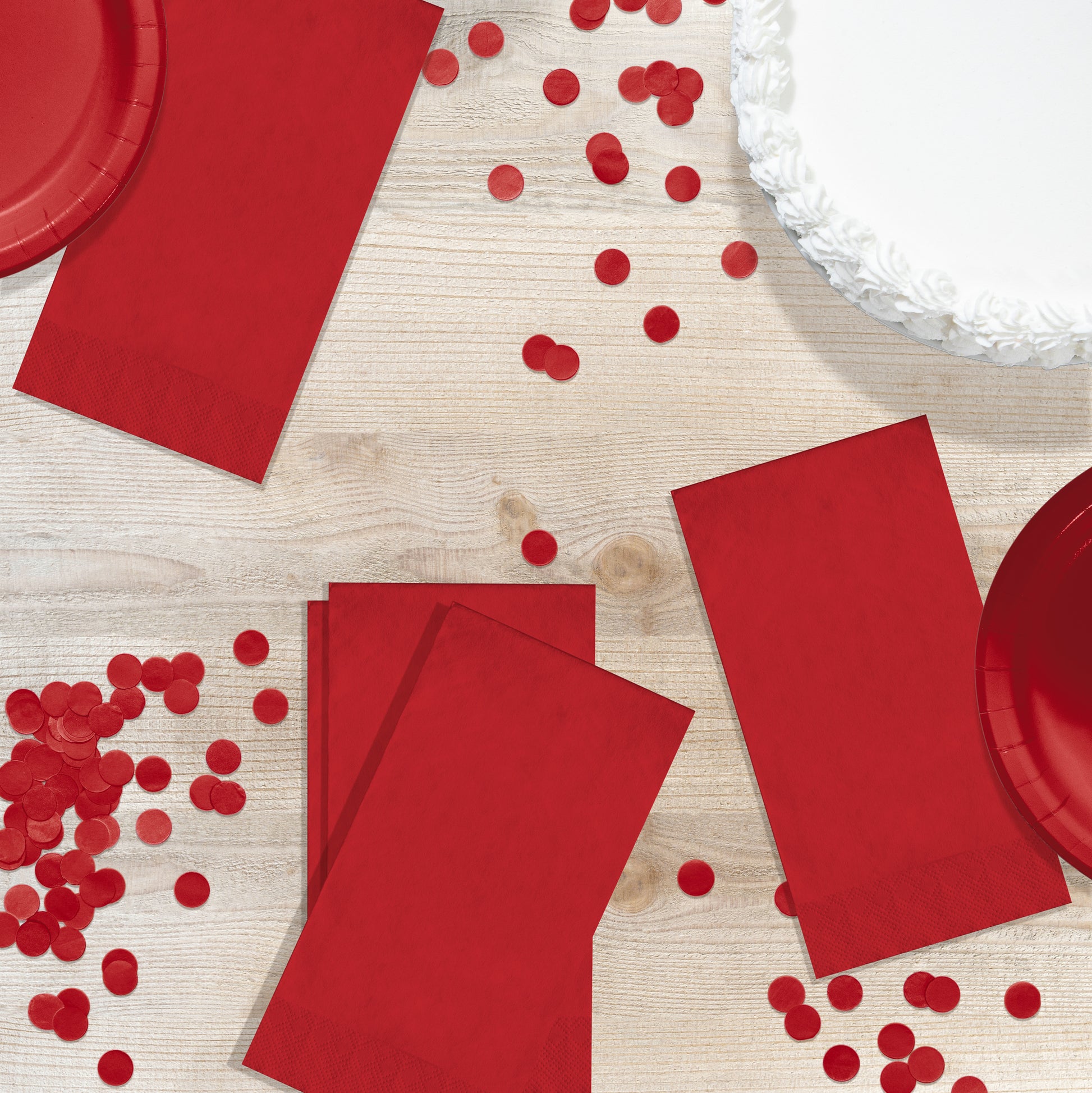 Red paper plates and napkins with scattered red confetti on a wooden surface