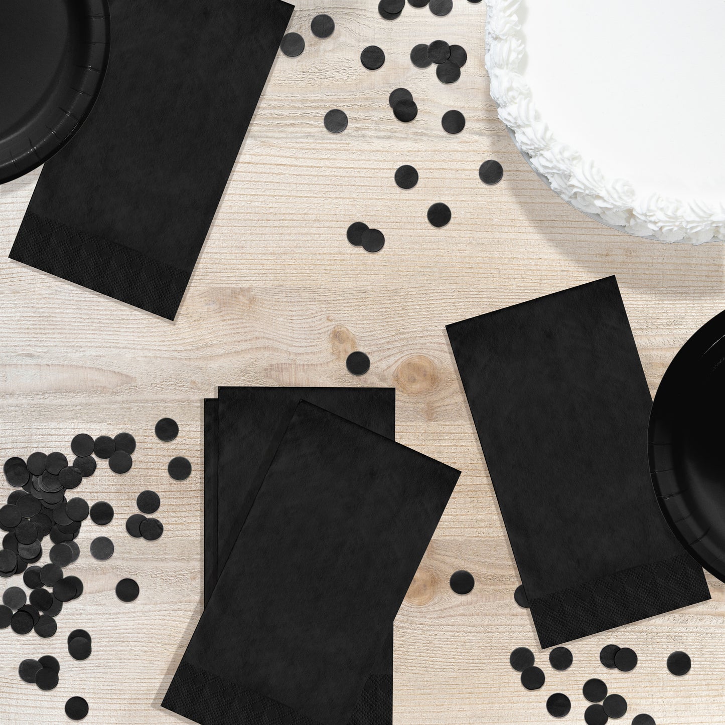 Black pin embossed guest napkins on a wood table with black circle confetti