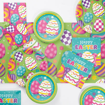 Easter-themed party supplies including plates and napkins displayed on a colorful egg designs tablecloth.