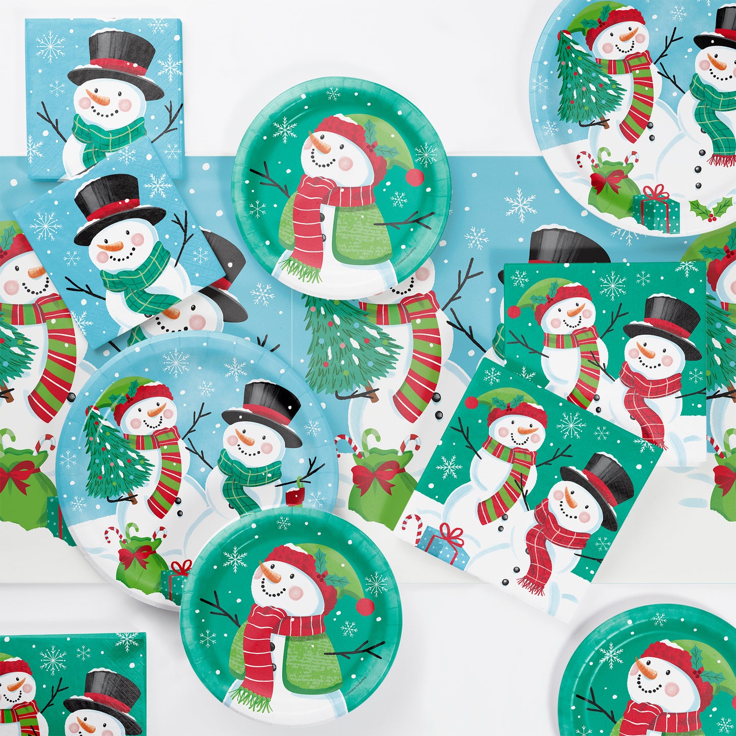 Paper napkins, plates and tablecloth featuring 2 snowmen, Christmas gifts, and snowflakes shown on a table.