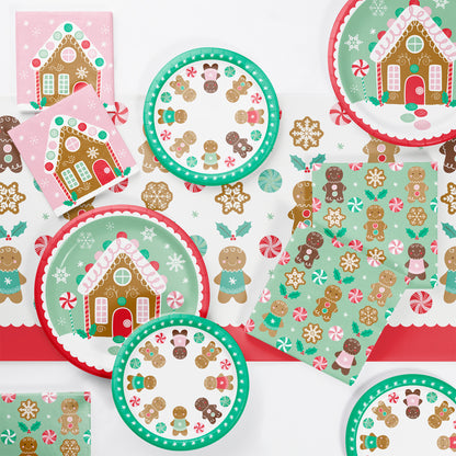 Christmas-themed paper plates, napkins and tablecloth with gingerbread house and candy cane designs on a white background.