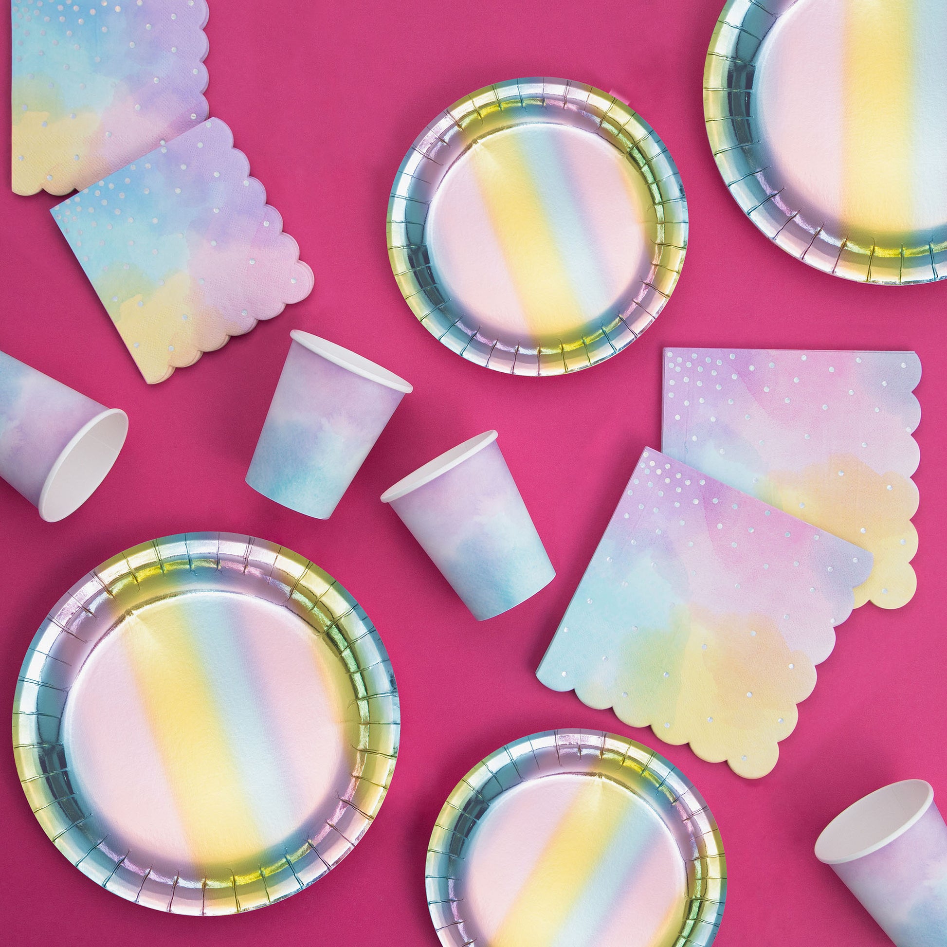 Iridescent paper plates, napkins, and cups on a hot pink background