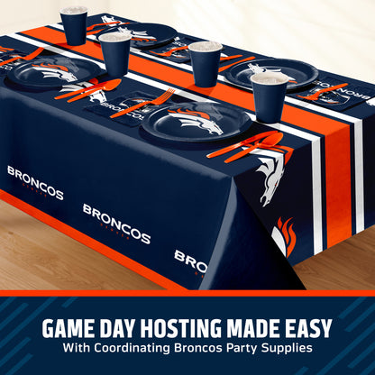 A table covered with Denver Broncos themed party supplies, including a navy blue tablecloth with orange and white stripes, matching plates, cups, and napkins. A text banner at the bottom reads 'GAME DAY HOSTING MADE EASY With Coordinating Broncos Party Supplies'.