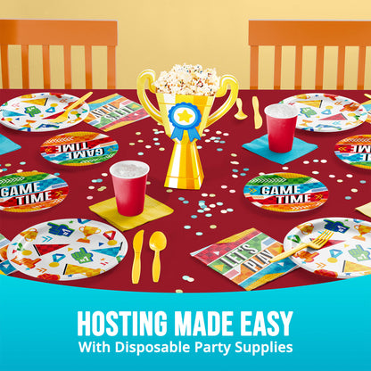 Disposable party supplies on a table with 'Game Time' plates, cups, and a trophy centerpiece.