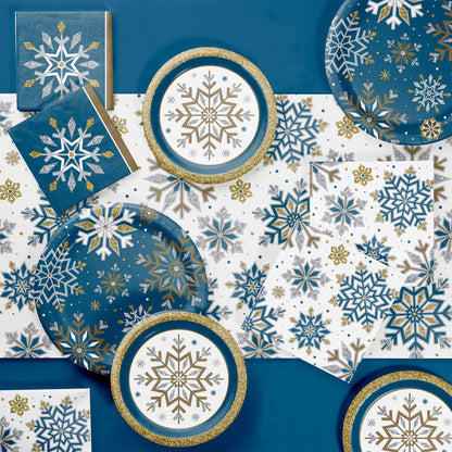 Paper napkins, plates and tablecloth with snowflake designs on blue, white, and gold background